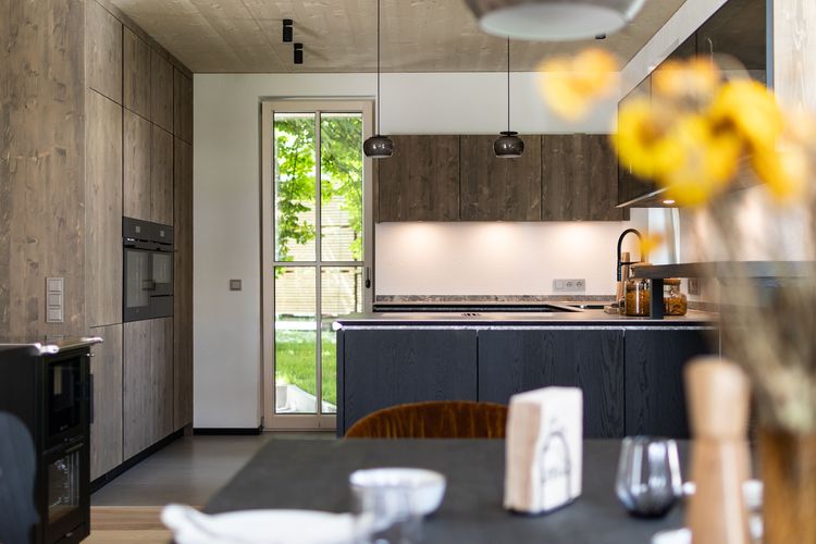 Der Blick vom Esszimmer auf die moderne Küche des modernen und großzügigen Holzhauses, bzw. Massivholzhauses im Landhausstil im Musterhauspark in Ortenburg. Der Neubau erinnert an die Chalets im Alpenvorland, hat aber viele moderne Designelemente.
